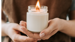 Glowing soy candle in an elegant glass jar on a rustic wooden table, casting a warm, eco-friendly glow in a cozy home setting.